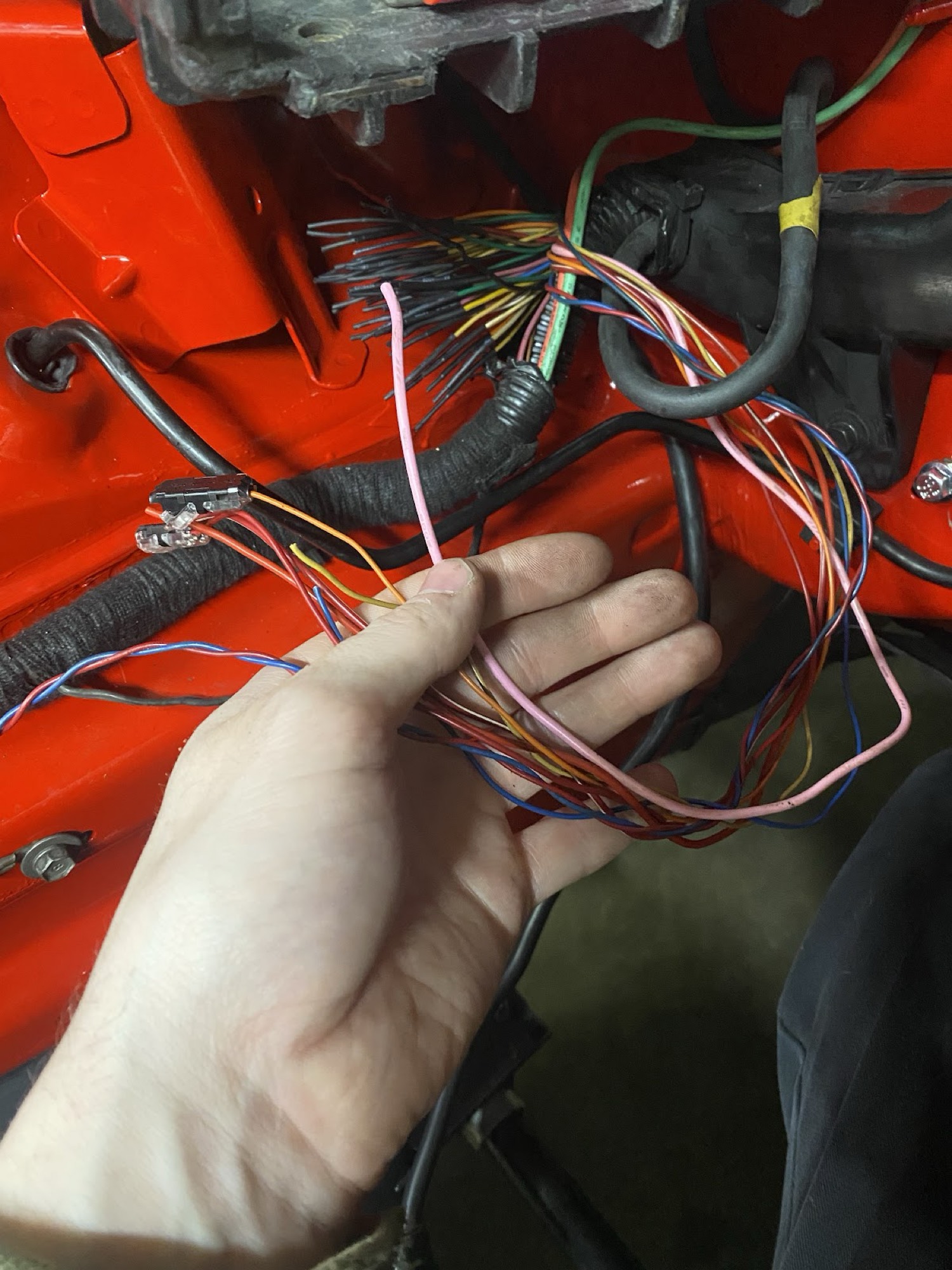 Hand holding pink starter wire and harness pulled from passenger fuse box